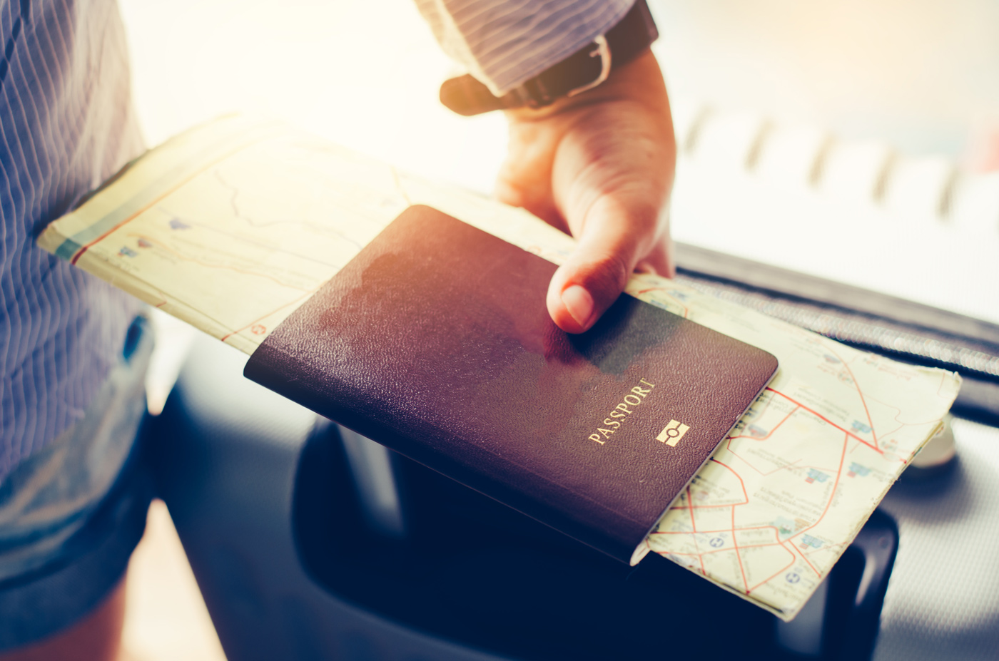 Ausschnitt von einer Hand, die einen Reisepass und eine Karte festhält