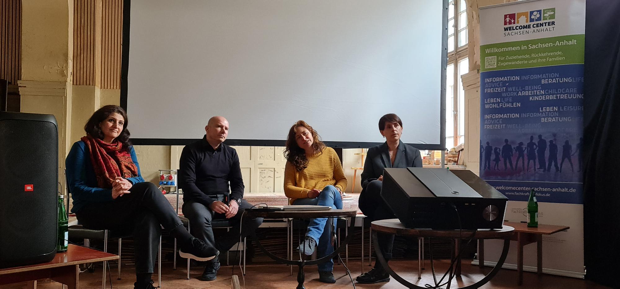 drei Frauen und ein Mann sitzen nebeneinander auf einem Podium
