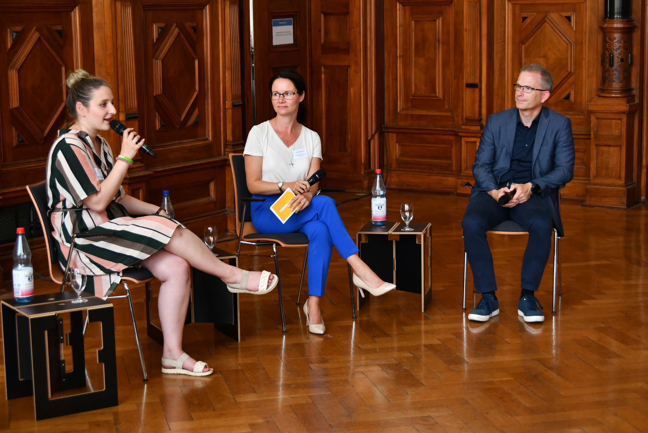 Drei Personen sitzen auf Stühlen und diskutieren miteinander