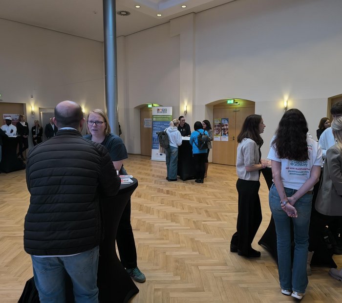 ein Raum mit mehreren Stehtischen, an denen sich kleine Gruppen unterhalten