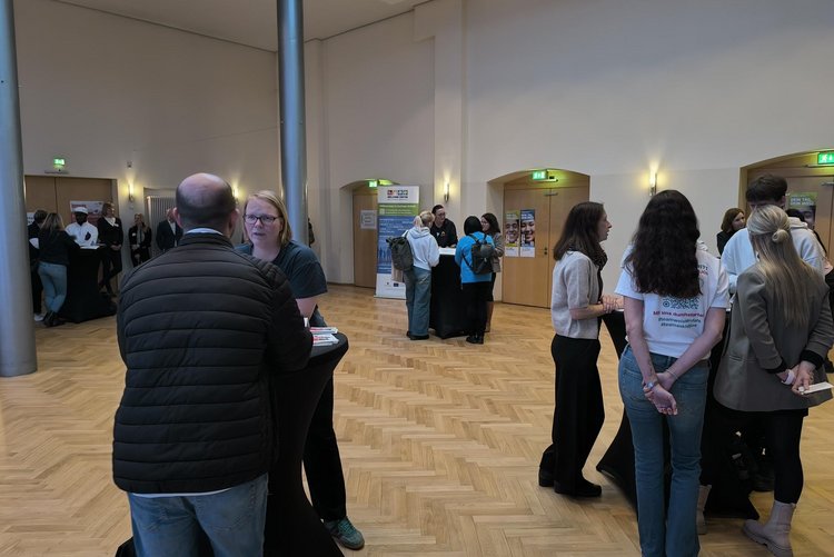 ein Raum mit mehreren Stehtischen, an denen sich kleine Gruppen unterhalten