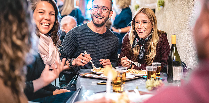 Eine Gruppe von jungen Menschen sitzt in einem Restaurant. Sie essen und lachen gemeinsam.