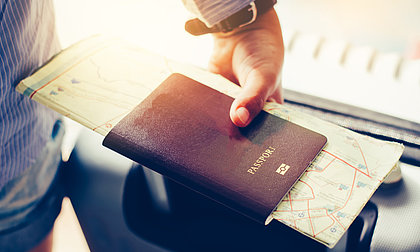 Ausschnitt von einer Hand, die einen Reisepass und eine Karte festhält