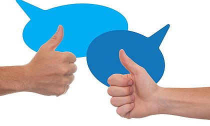 zwei Hände mit dem Handzeichen "Daumen hoch" vor zwei blauen Sprechblasen