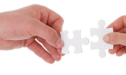 zwei Hände führen zwei Puzzleteile zusammen