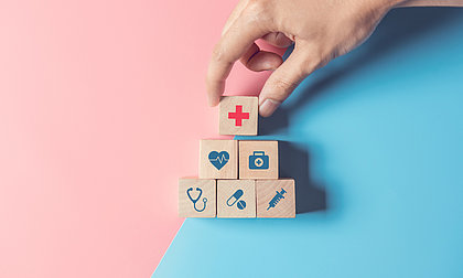 Kleine hölzerne Quadrate mit Symbolbildern für Gesundheit: rotes Kreuz, Herz, Stethoskop, Pillen, Spritzte
