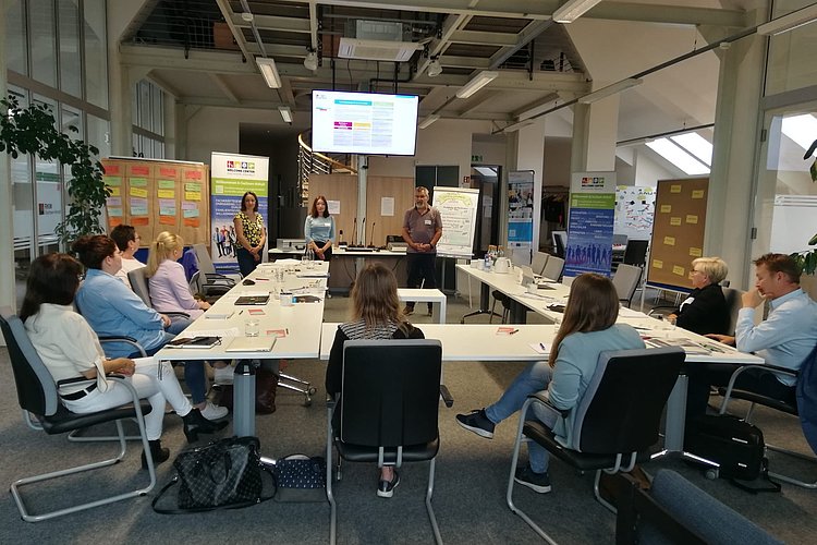 Vortragende und Zuhörende in einem Workshop-Raum