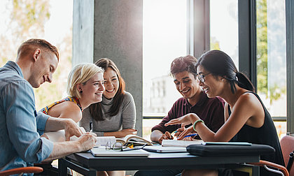 5 Menschen sitzen und arbeiten zusammen an einem Tisch, sie wirken glücklich