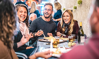 Eine Gruppe von jungen Menschen sitzt in einem Restaurant. Sie essen und lachen gemeinsam.