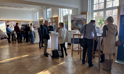 sich unterhaltende Menschen in einem lichtdurchfluteten Veranstaltungsraum mit mehreren Stehtischen und Roll-ups