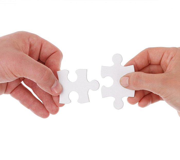 zwei Hände führen zwei Puzzleteile zusammen