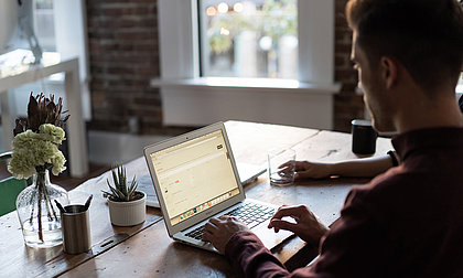 Mann sitzt am Schreibtisch und schreibt etwas am Laptop